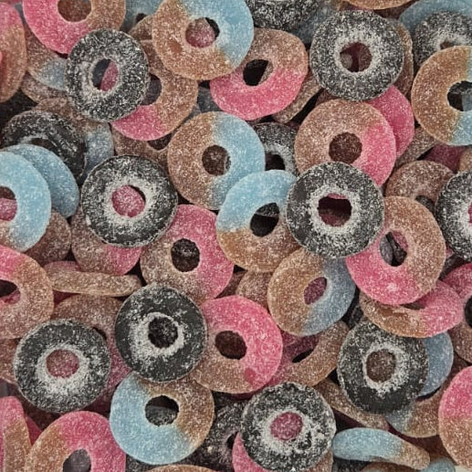 A clear plastic tub filled with colorful ring-shaped candies, including pink, blue, brown, and dark gray/sugar-coated pieces, photographed from above on a white surface.