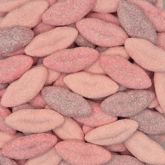 A clear plastic square container filled with small, oval-shaped, sugar-coated candies in shades of pink and light purple, photographed from a top-down perspective on a light gray surface.