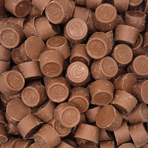 A clear plastic tub filled with many small round milk-chocolate candies, photographed from above on a white surface.