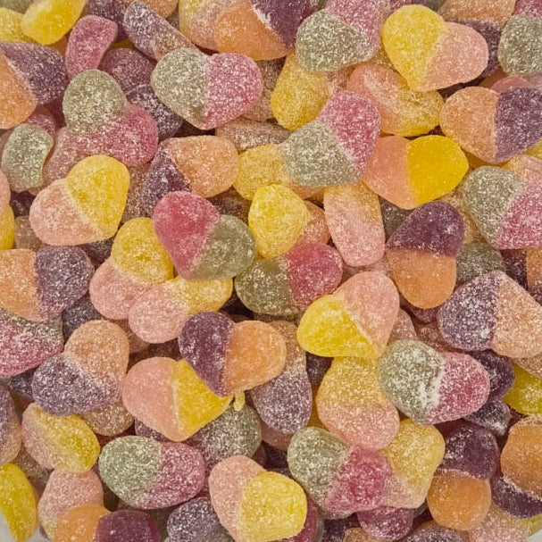 A clear plastic tub filled with small, heart-shaped, sugar-coated candies in assorted pastel colors including pink, yellow, orange, green, and purple, photographed from above on a white surface.