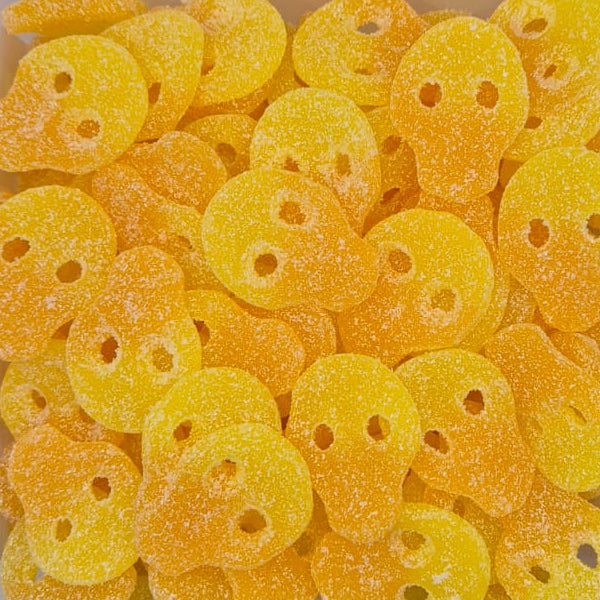 A clear plastic container filled with small, round, yellow-orange gummy candies coated in sugar, photographed from above on a plain light background.