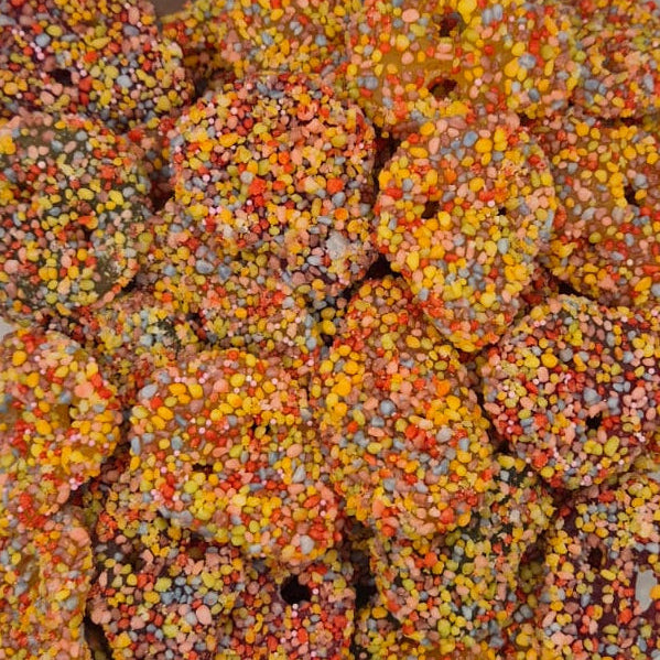 A clear plastic container filled with small ring-shaped pastries or cookies heavily coated in multicolored sprinkles, photographed from above on a plain light background.