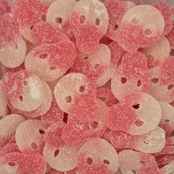 Pink and white sugar-coated skull-shaped candies piled in a clear plastic container, photographed from above on a plain light background.