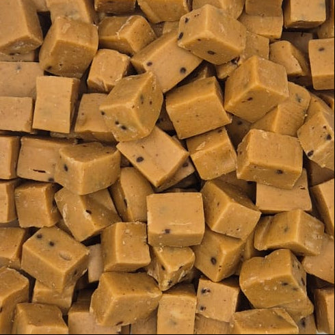 Cubical pieces of golden-brown fudge or caramel candy arranged in a clear plastic container on a white surface.