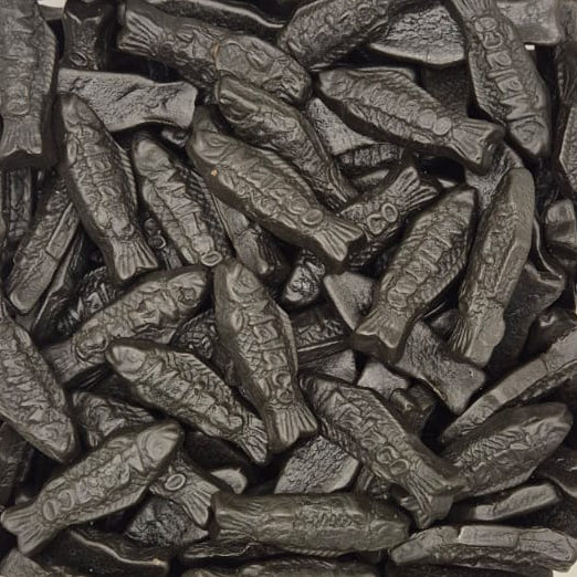 A clear plastic square container filled with many small dark gray to black fish-shaped items, photographed from above on a white surface.