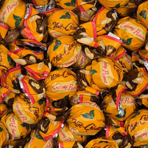 A clear plastic tub filled with individually wrapped yellow-orange chocolates, photographed from above on a white surface.