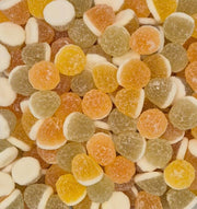 A close-up, top-down view of assorted round gummy candies in orange, yellow, green, and white, densely packed together.