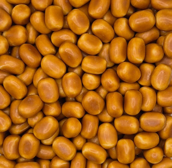 A close-up, top-down view of many glossy, golden-brown, bean-shaped Swedish candies or sweets filling the entire frame.