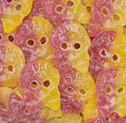 A close-up pile of sugar-coated skull-shaped candies in a yellow and pink gradient, with small dark eye cutouts visible.