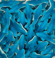 A close-up pile of blue shark-shaped gummy candies with white edges, filling the entire frame.