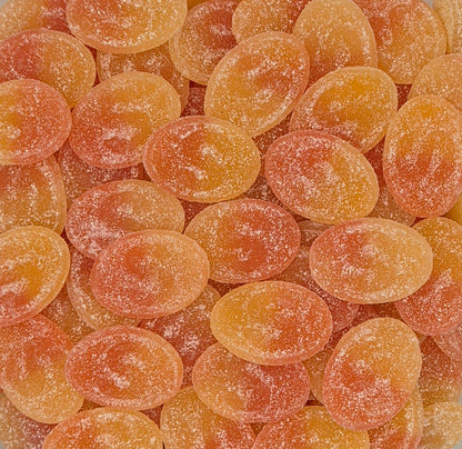 A close-up pile of oval-shaped, sugar-coated gummy candies in shades of orange and peach.