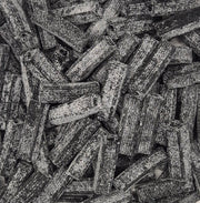 A close-up, top-down view of a pile of dark brown textured pasta sticks, likely fusilli or penne, with a rough, speckled surface.