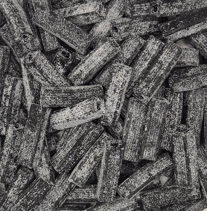 A close-up, top-down view of a pile of dark brown textured pasta sticks, likely fusilli or penne, with a rough, speckled surface.