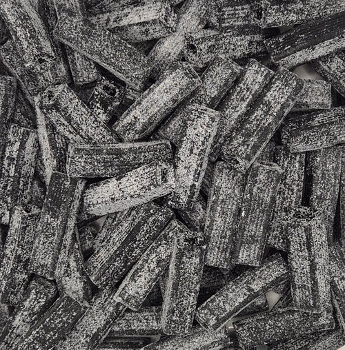 A close-up, top-down view of a pile of dark brown textured pasta sticks, likely fusilli or penne, with a rough, speckled surface.