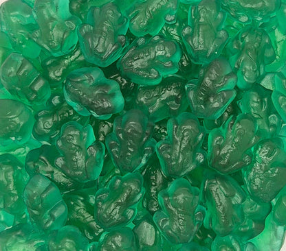 A close-up pile of translucent green gummy candies shaped like frogs, filling the entire frame.