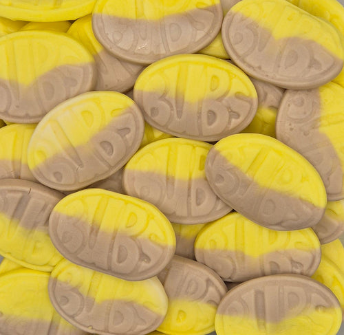 A close-up pile of oval candies with a two-tone yellow and light brown color scheme and embossed lettering.