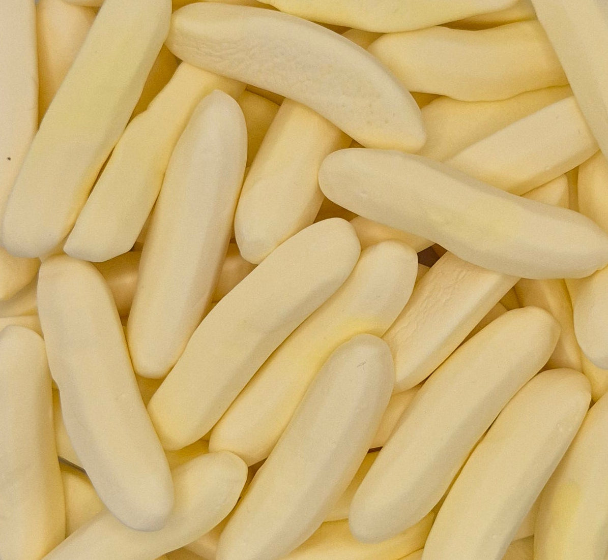 A close-up pile of pale yellow, curved, stick-like pieces, likely wax melts or soap bars, filling the entire frame.