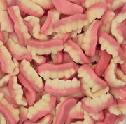 Pink and white wavy candy pieces, resembling gummy worms or worms with teeth, piled in a clear plastic square container.