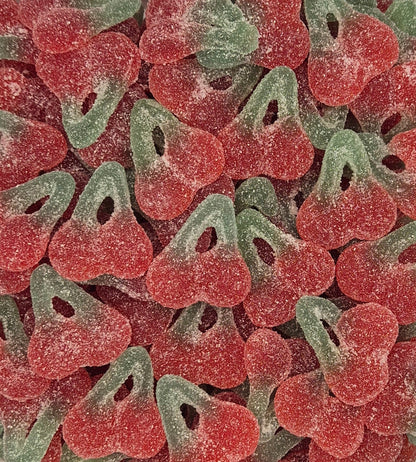 A close-up pile of cherry-shaped sour gummy candies coated in white sugar powder, showing alternating red and green halves.