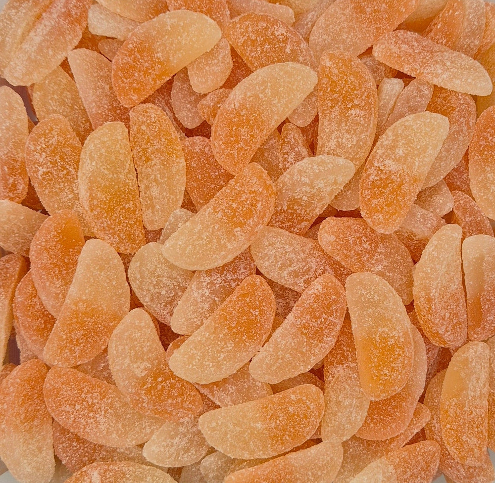 A close-up pile of translucent orange citrus candy pieces coated with sugar, filling the entire frame.