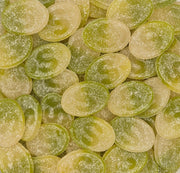 A close-up pile of oval translucent candies in pale yellow-green and light green tones, with a frosted sugar-like coating.