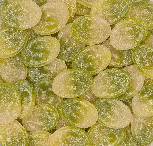 A close-up pile of oval translucent candies in pale yellow-green and light green tones, with a frosted sugar-like coating.