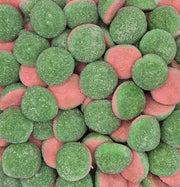A clear plastic square container filled with round, sugar-coated candy discs in green and pink, photographed from above against a plain light background.
