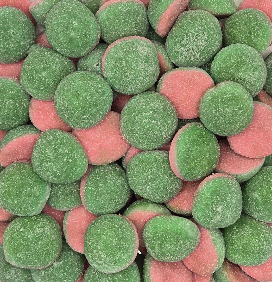 A clear plastic square container filled with round, sugar-coated candy discs in green and pink, photographed from above against a plain light background.