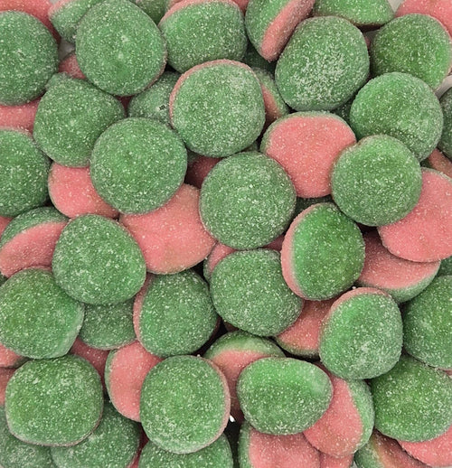 A clear plastic square container filled with round, sugar-coated candy discs in green and pink, photographed from above against a plain light background.
